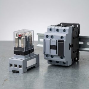 comparación de tamaño entre un relé de control enchufable y un contactor trifásico sobre una mesa de trabajo. 1